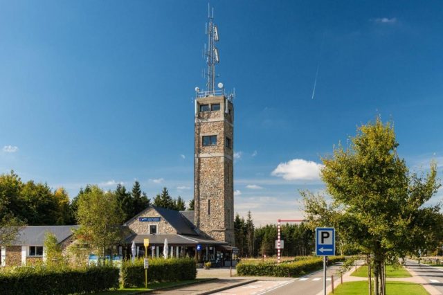 La tour d’observation en pierre du Signal de Botrange et le bâtiment d’accueil, sous un ciel bleu.