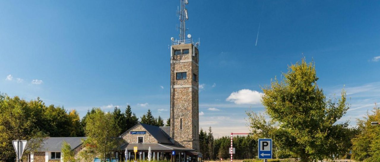 La tour d’observation en pierre du Signal de Botrange et le bâtiment d’accueil, sous un ciel bleu.